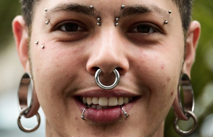 Close-up portrait of a young man showcasing a variety of unique facial piercings and jewelry.