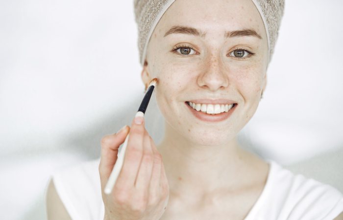Close-up of a smiling woman applying makeup with a brush, enhancing natural beauty.