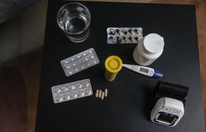 Top view of various medications, tablets, and medical devices on a table with a glass of water.