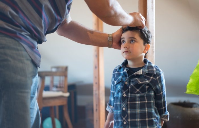 A father marking his young son's height on a wooden pole indoors, capturing a family bonding moment.