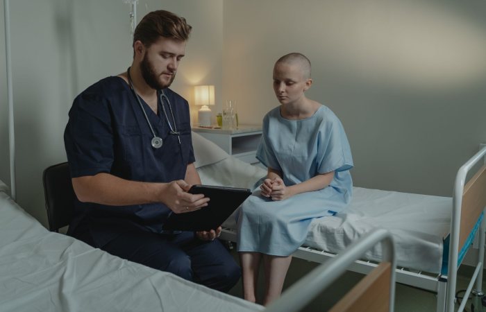 A doctor in a hospital ward consulting a patient with a digital tablet.