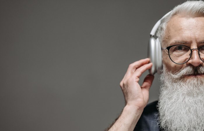 Close-up of a senior man with a beard and glasses, listening to music with headphones.