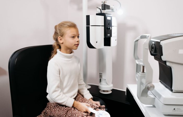 A young girl sits for an eye test using optical instruments in a medical facility.