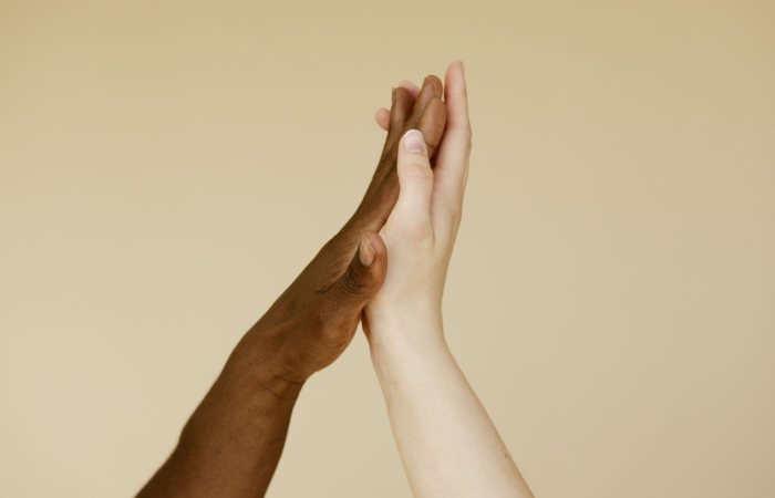 Close-up of diverse hands giving a high five on a beige background, symbolizing unity and diversity.