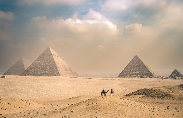 Explore the majestic Pyramids of Giza under a sunny sky with distant travelers on camels.