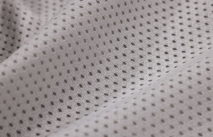 Macro shot of white mesh textile displaying intricate weave pattern, ideal for sportswear.